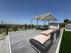 Eine Holzterrasse mit überdachter Sitzgelegenheit und Blick auf die Landschaft.