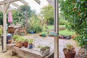 Ein überdachter Patio-Bereich mit einer Holzbank, Topfpflanzen und einem Tisch mit Stühlen.