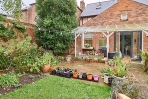 Ein Backsteinhaus mit überdachter Terrasse, Kübelpflanzen und einem Garten.