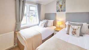 Ett hotellrum med två sängar, ett fönster med gardiner, ett element, en lampa och en tavla på väggen.