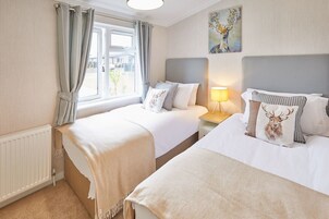 A hotel room with two beds, a window with curtains, a radiator, a lamp, and a painting on the wall.