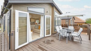 Ett modernt hus med en veranda, en matplats med stolar och ett kök som syns genom den öppna dörren.