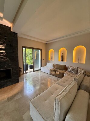 A spacious living room with a stone fireplace, a large sectional sofa, a coffee table, and a sliding glass door leading to an outdoor area.