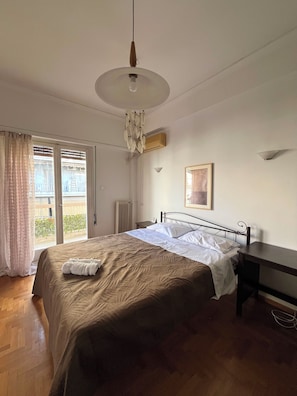 Ein Schlafzimmer mit Bett, Schreibtisch, Pendelleuchte, Heizkörper und einem Fenster mit Vorhängen.