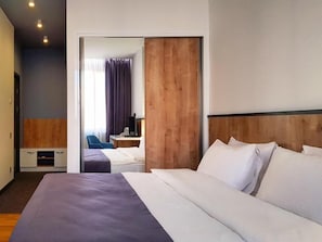 Una habitación de hotel moderna con una cama grande, un cabecero de madera, un escritorio con una silla y vistas a través de una puerta.