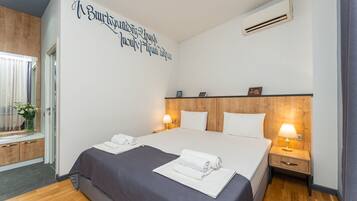 Quarto de hotel com uma cama grande, duas mesas de cabeceira com luminárias, uma cabeceira de madeira e uma parede com texto.