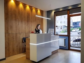 A reception desk with a modern design, a wooden wall, and a view of the street outside.