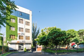 Un edificio de hotel con fachada moderna, entrada visible y zona de estacionamiento al frente.