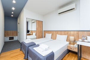 Habitación de hotel con dos camas, un escritorio, un espejo, aire acondicionado y un baño pequeño.