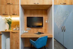 A compact room with a wooden desk, a blue chair, a television, and a refrigerator with decorative etching. - Alpha by Horizon Hotels, Yerevan  (Yerevan)