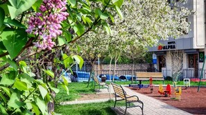 A park area with benches, playground equipment, and a building with a sign that reads 'HOTEL ALPHA'. - Alpha by Horizon Hotels, Yerevan  (Yerevan)