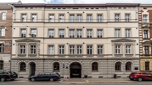 A multi-story building with a symmetrical facade, large windows, and a central entrance with an archway. - RentPlanet - Apartament Gliwicka (Katowice)