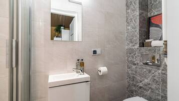 A modern bathroom with a glass shower enclosure, a white sink, and marble walls.