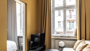A hotel room with a bed, a TV, a small table, and a window with curtains. - RentPlanet - Apartament Gliwicka (Katowice)
