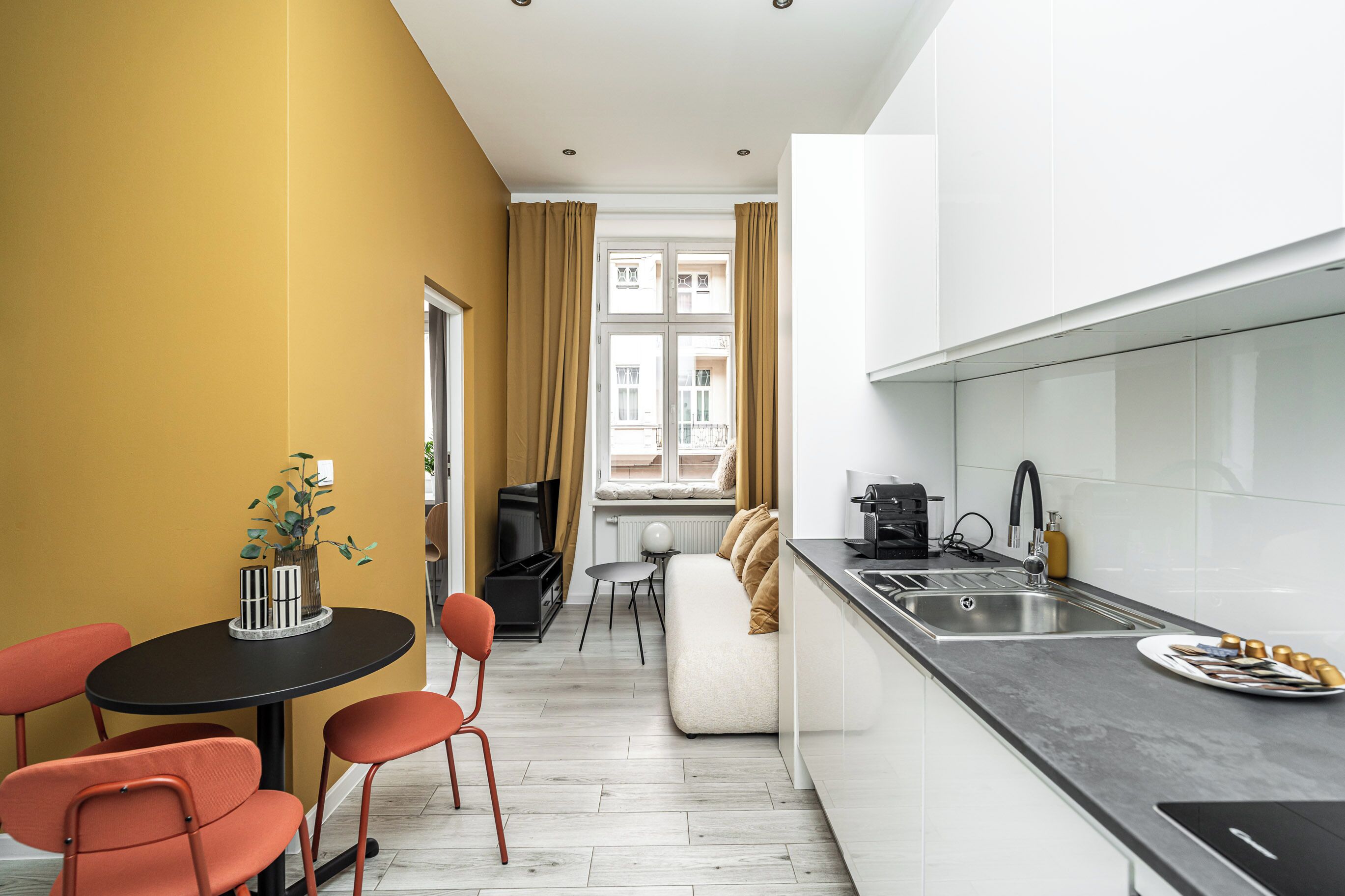 A compact kitchen with a dining area, a sofa, and a TV.