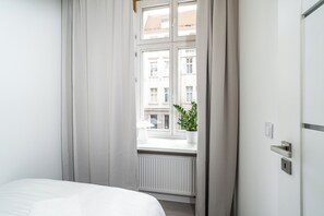 Een hotelkamer met een bed, een raam met gordijnen, een radiator en een potplant.