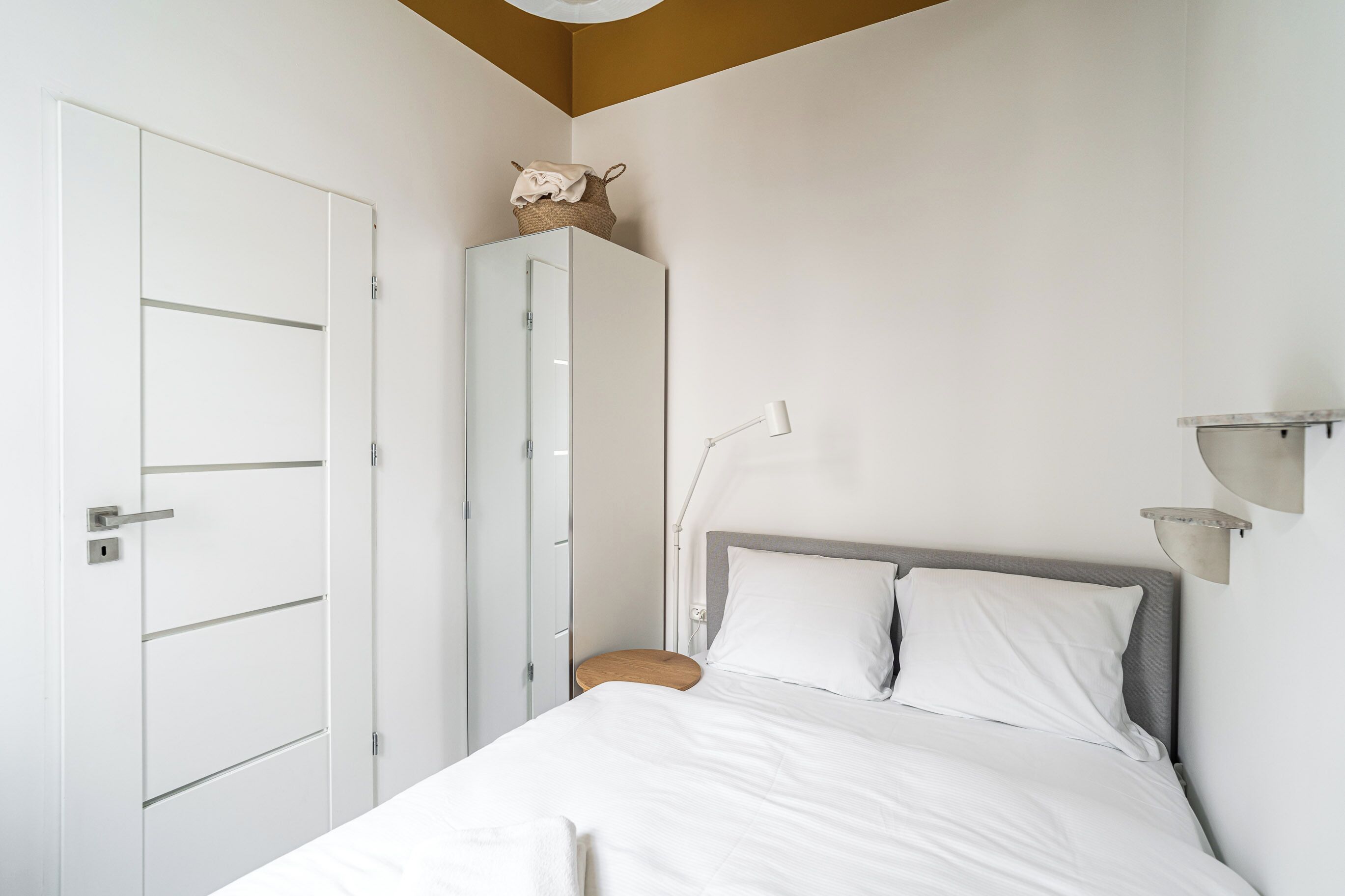 A bedroom with a bed, a wardrobe, a nightstand, and a wall-mounted lamp.
