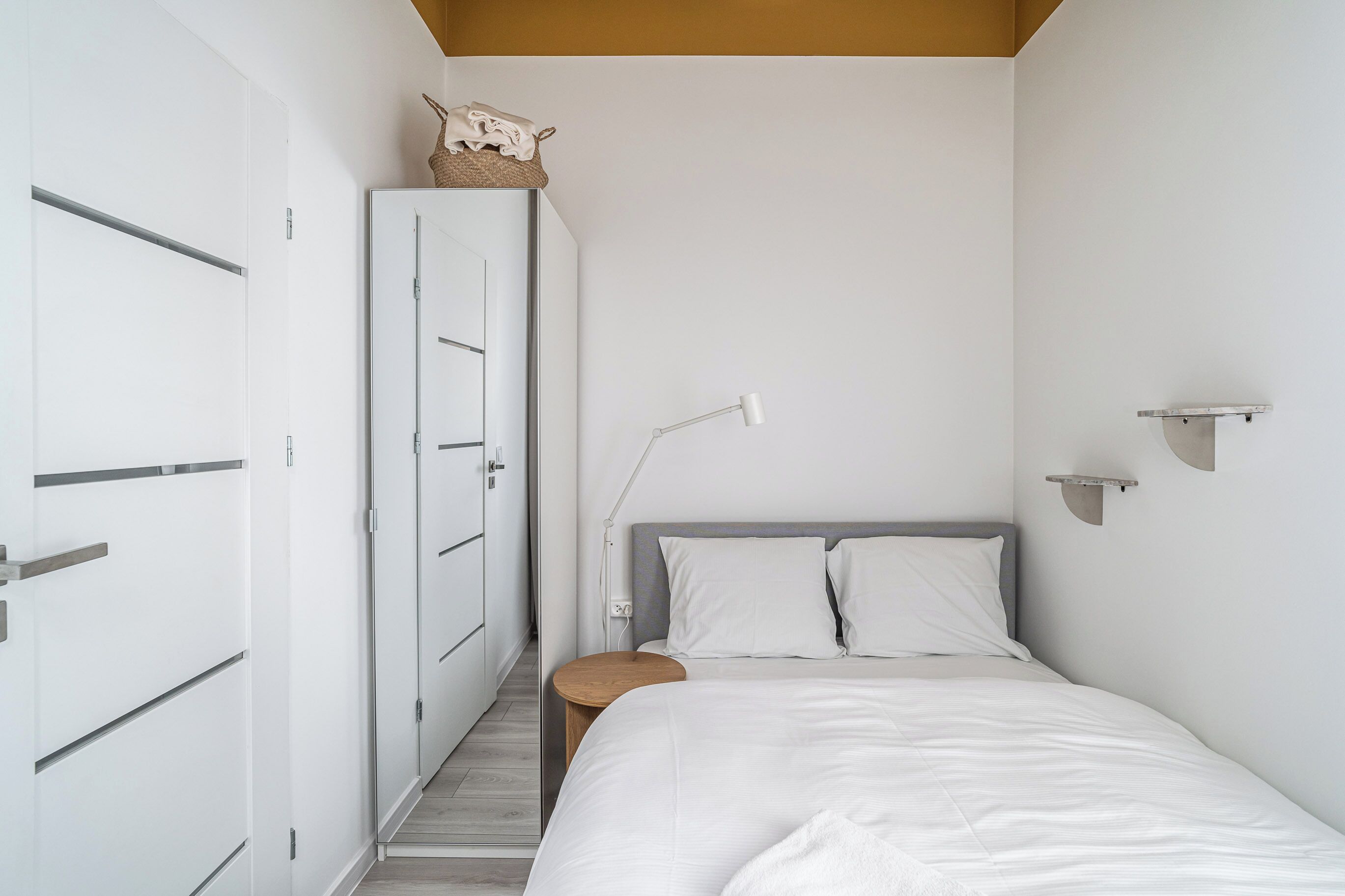 A bedroom with a bed, bedside table, lamp, wardrobe, and a small shelf.