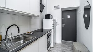 A compact kitchen with a sink, stove, microwave, and a small refrigerator. - RentPlanet - Apartament Gliwicka (Katowice)