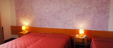 Habitación de hotel con dos camas, cada una con una colcha roja y un cabecero de madera. Hay mesitas de noche con lámparas y un teléfono.