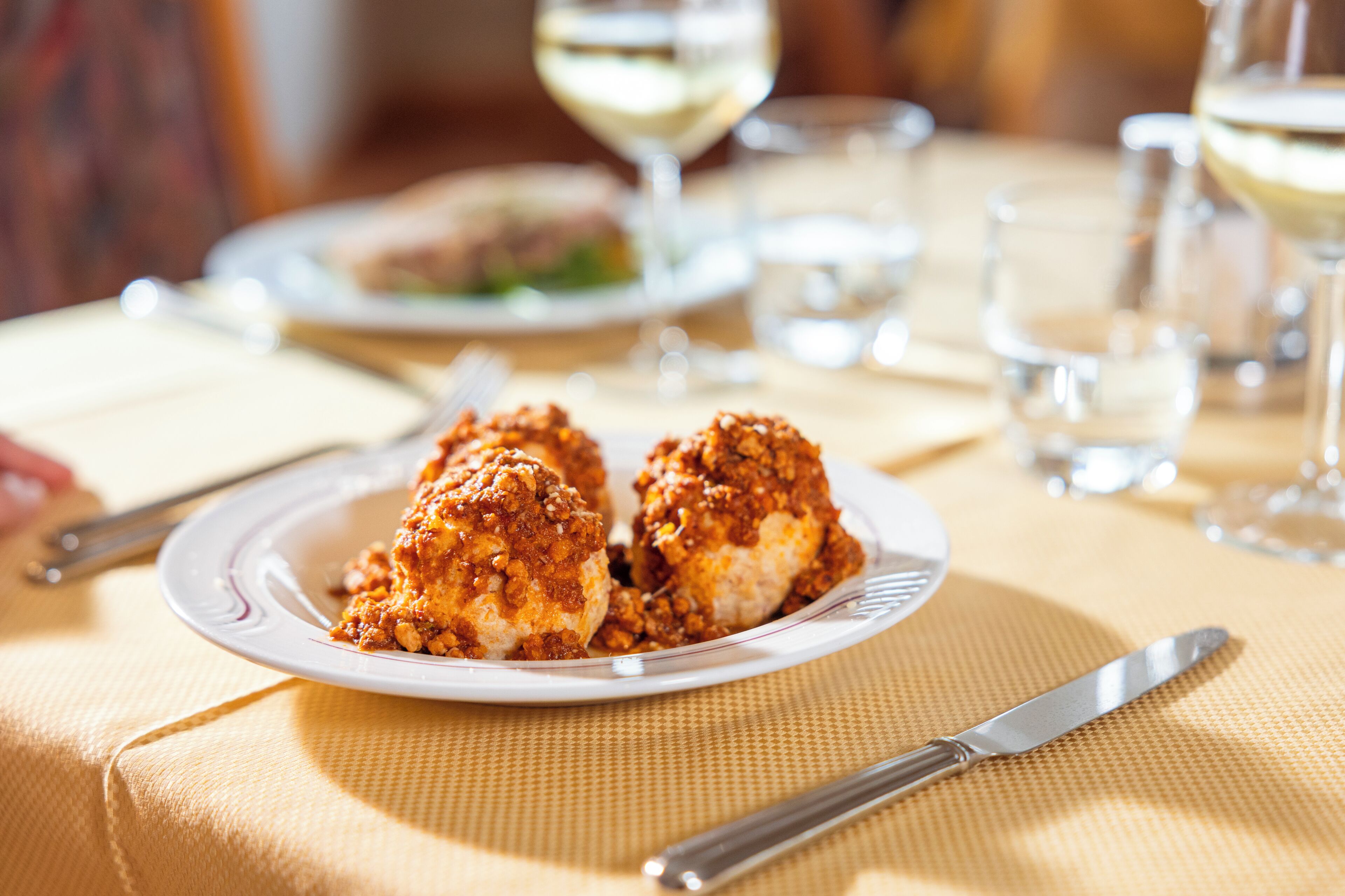 A dining table with a plate of food, a knife, and a glass of white wine.