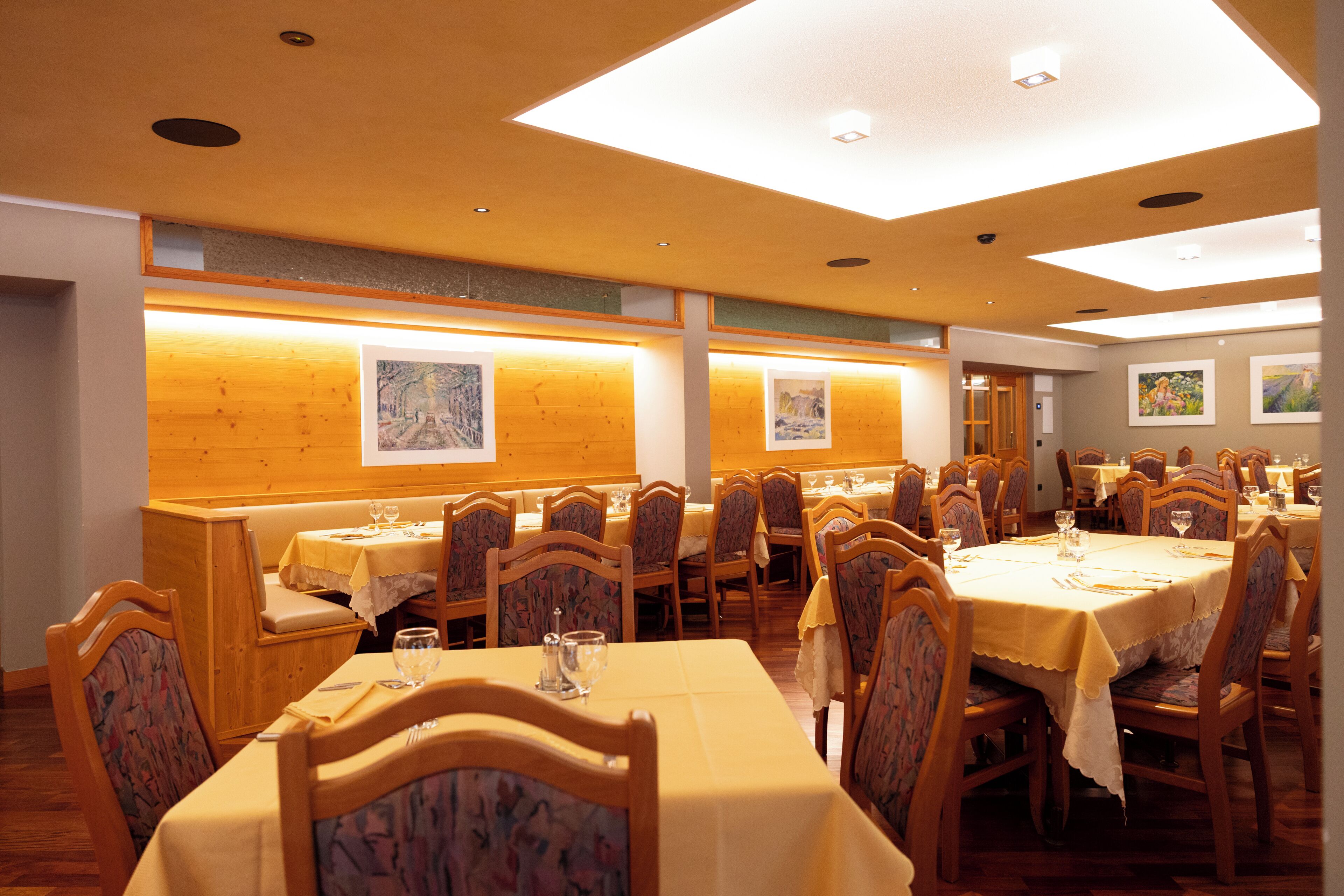 A dining area with multiple tables and chairs, wooden paneling on the walls, and framed artwork.