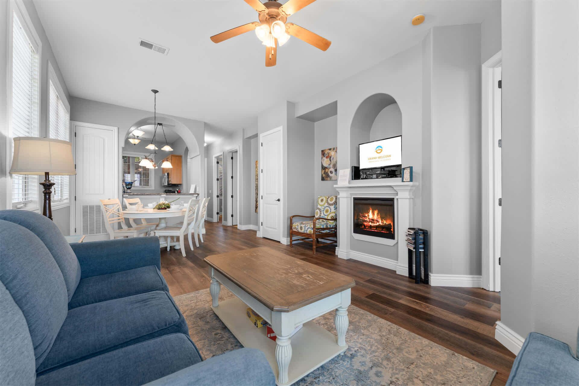 A spacious living room with a fireplace, a dining area, and a kitchen in the background.
