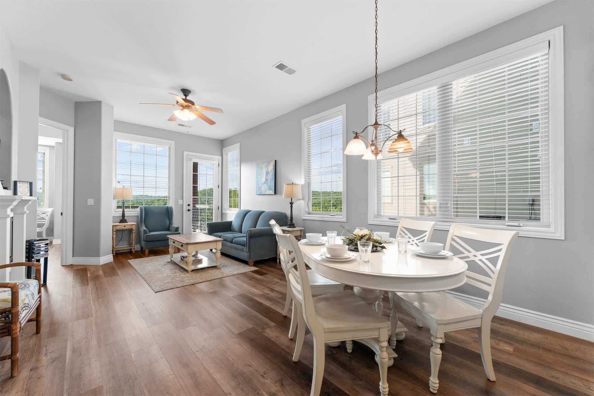 A spacious living room with a dining area, large windows, and a ceiling fan.