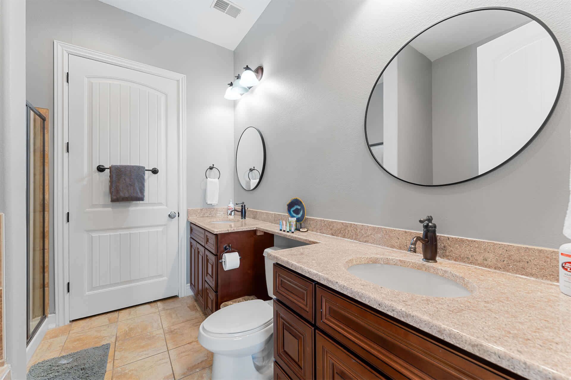 A bathroom with a white door, a sink with a vanity, a toilet, and two wall-mounted mirrors.
