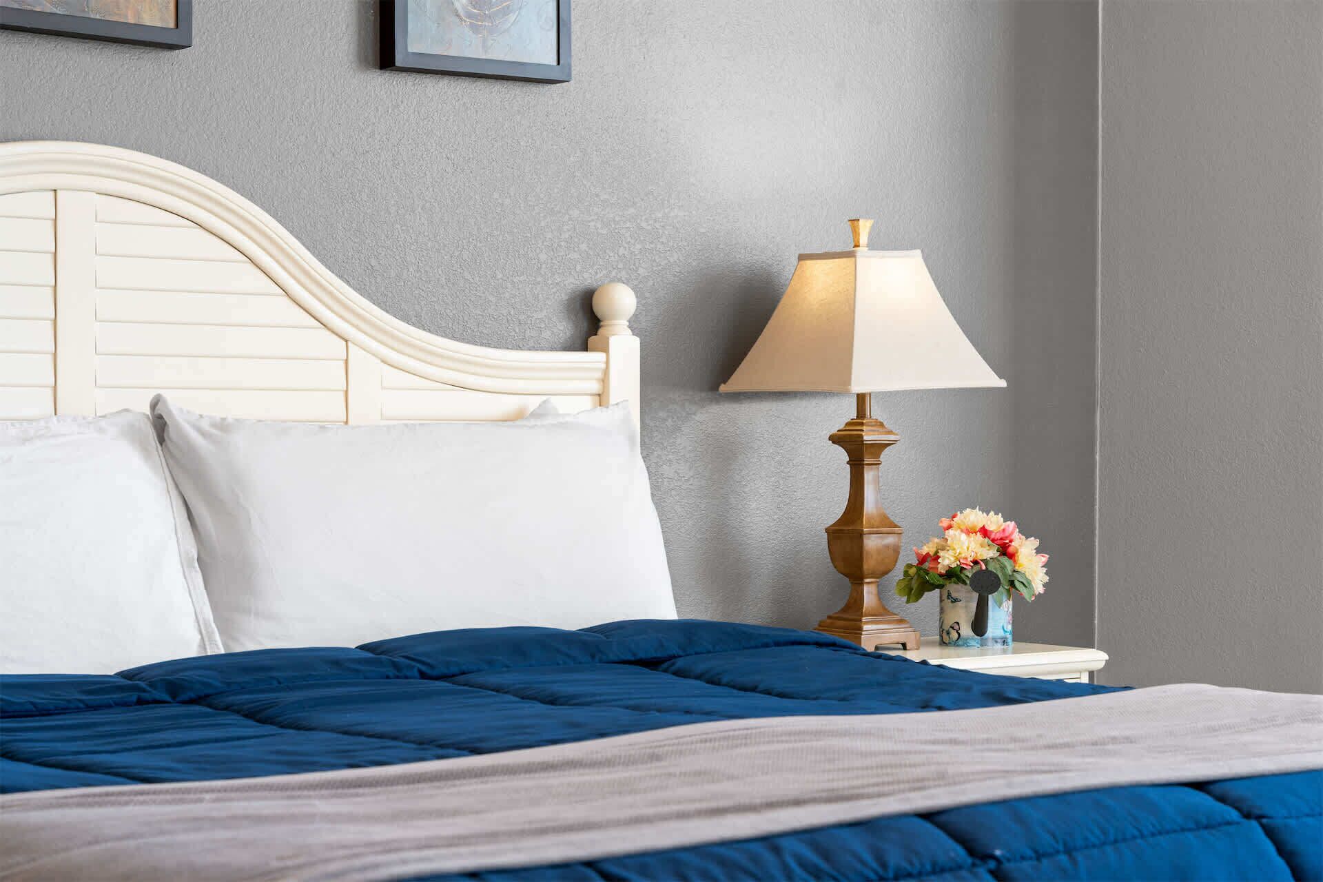 Een keurig opgemaakt bed met een blauwe deken, een wit kussen en een houten hoofdbord.