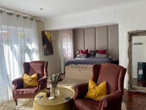 Ein Schlafzimmer mit einem Bett, zwei Sesseln, einem runden Couchtisch und einem großen Spiegel.