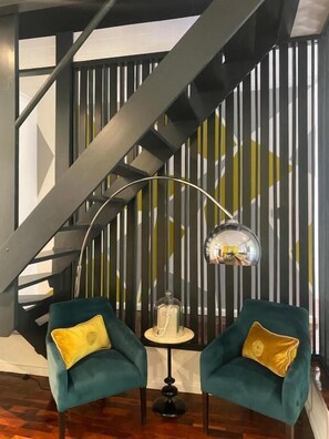 Ein modernes Interieur mit einer Treppe, zwei smaragdgrünen Sesseln mit gelben Kissen, einem kleinen runden Tisch und einer Stehlampe.