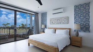 A bedroom with a large bed, a nightstand, a chair, a balcony with a view of palm trees, and patterned walls. - Lancaster Mews 1 (Westmoreland)