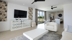 A modern living room with a white sofa, a white coffee table, a TV, and a dining area with a kitchen in the background. - Lancaster Mews 1 (Westmoreland)