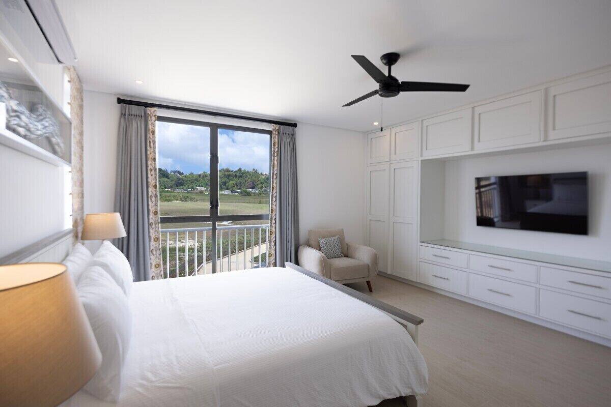 A hotel room with a bed, a TV, a ceiling fan, a balcony with a view, and a chair.