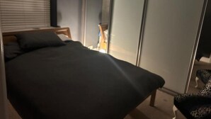 A bed with a dark cover, a wooden headboard, and a nightstand with a lamp. - House - Central Stamford - Sleeps 4 - Parking (Stamford)
