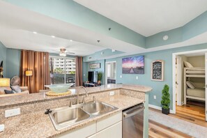 Eine moderne Küche mit Granit Arbeitsplatten, Spüle aus Edelstahl und Geschirrspüler. Es gibt einen Essbereich mit Tisch und Stühlen, einen Deckenventilator und einen Blick auf einen Balkon.