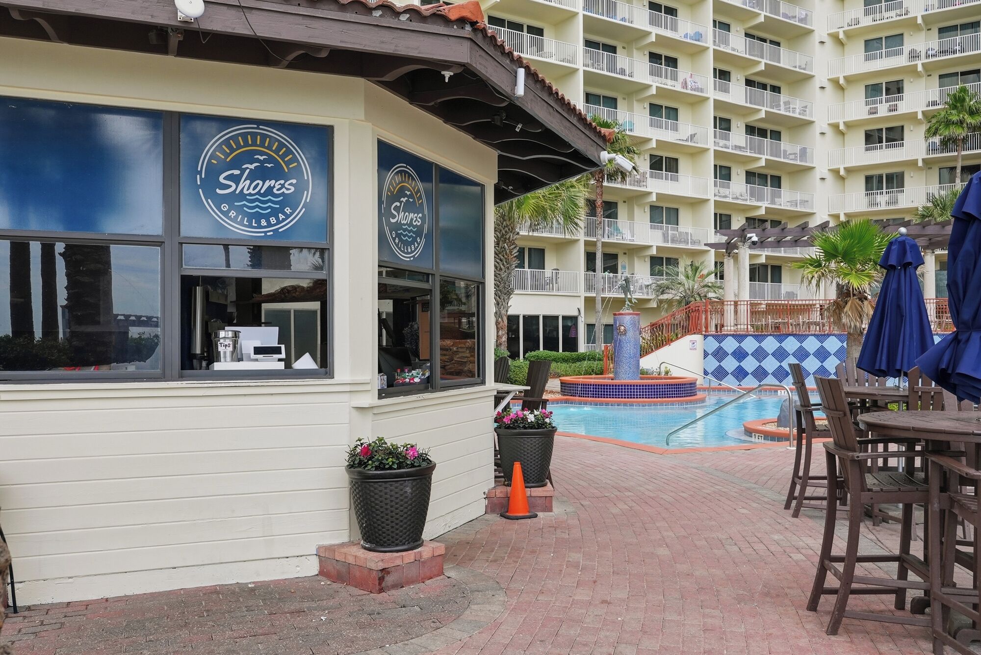 A restaurant with a poolside area, including a pool, lounge chairs, and a building with balconies.
