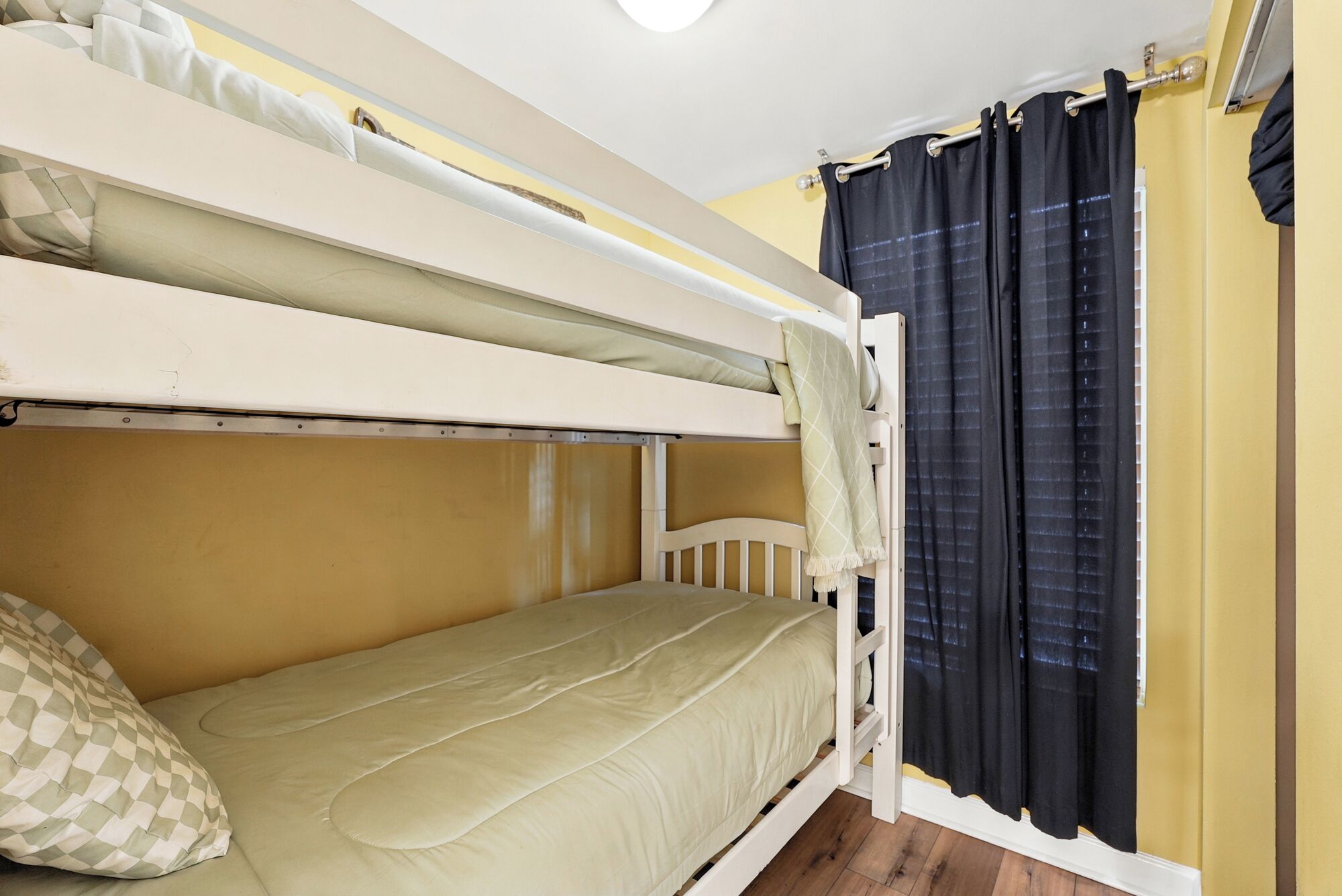 Habitación con literas, una ventana, cortinas y almohada de estampado vichy.