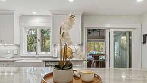 Una cocina moderna con armarios blancos, una encimera de mármol y una orquídea en maceta.
