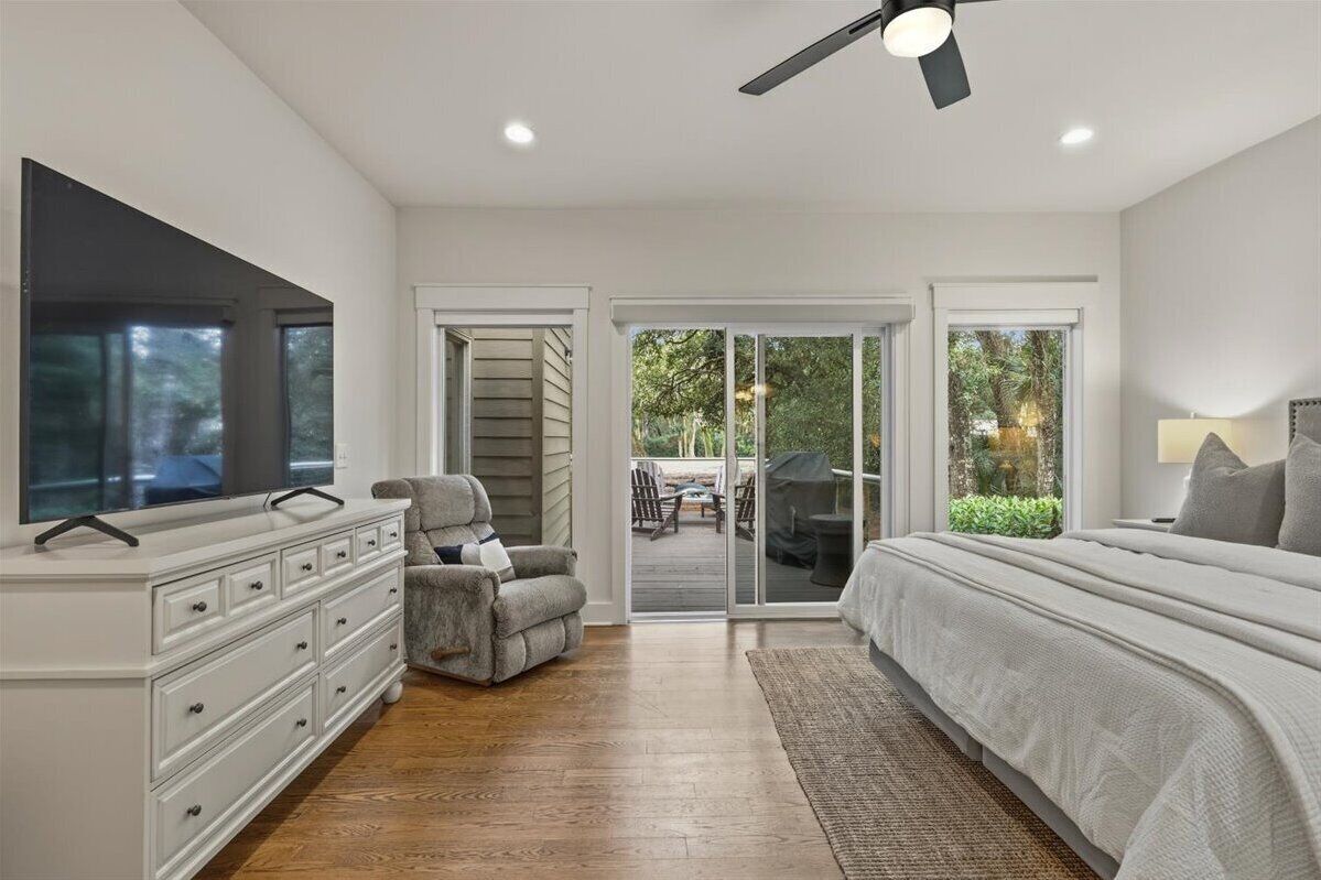A bedroom with a bed, a TV, a chair, a dresser, and a sliding glass door leading to an outdoor patio.
