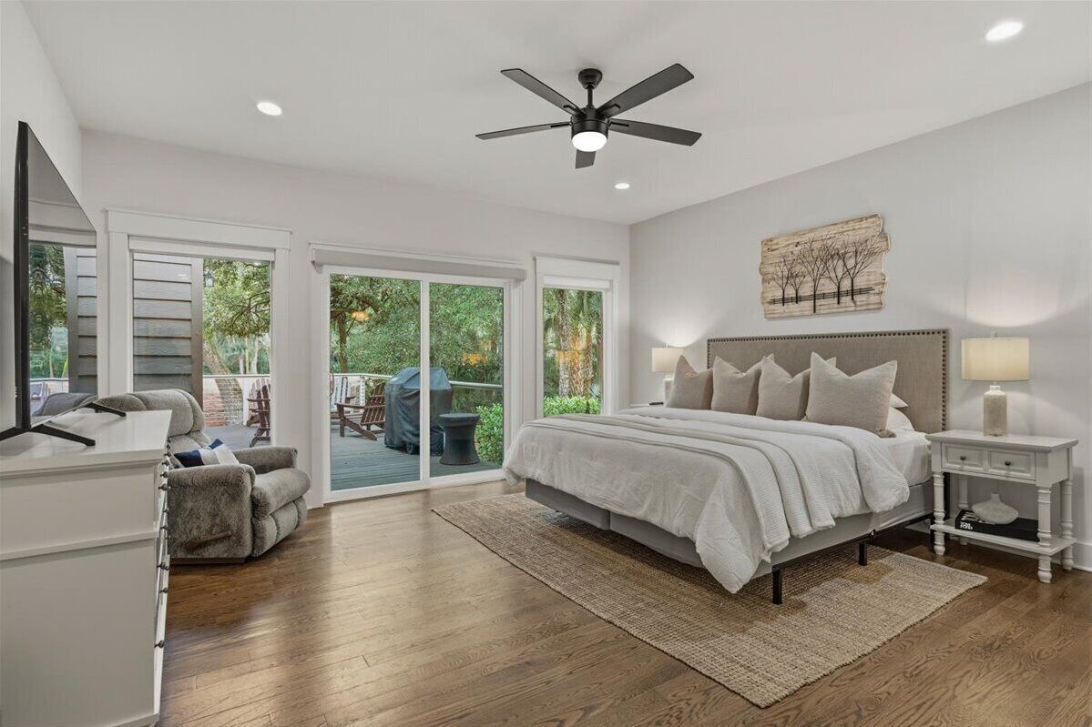 A bedroom with a bed, nightstands, a ceiling fan, and a view through a sliding glass door to an outdoor patio.