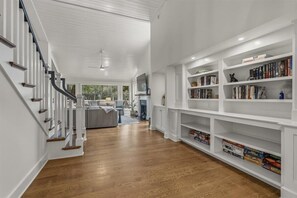 Ein geräumiger Flur mit einer Treppe, einem Wohnbereich mit einer Couch und einem Bücherregal voller Bücher.