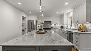 Una cocina moderna con una isla grande, armarios blancos y un refrigerador de acero inoxidable.