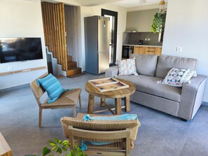 Ein modernes Wohnzimmer mit Sofa, Couchtisch, Fernseher und Küchenzeile mit Kühlschrank und Backofen.