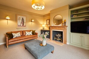 A living room with a brown leather sofa, patterned ottoman, wall-mounted lamps, a fireplace, and a green bookshelf. - Host Stay Tree Tops (Darlington)
