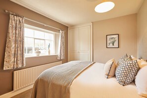 A bedroom with a large bed, a window with curtains, a radiator, and a framed botanical illustration on the wall. - Host Stay Tree Tops (Darlington)