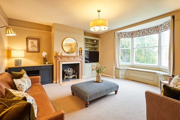 A living room with a sofa, ottoman, fireplace, and a large window with a view. - Host Stay Tree Tops (Darlington)