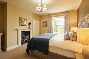 Un dormitorio con cama, chimenea, ventana con cortinas y candelabro.