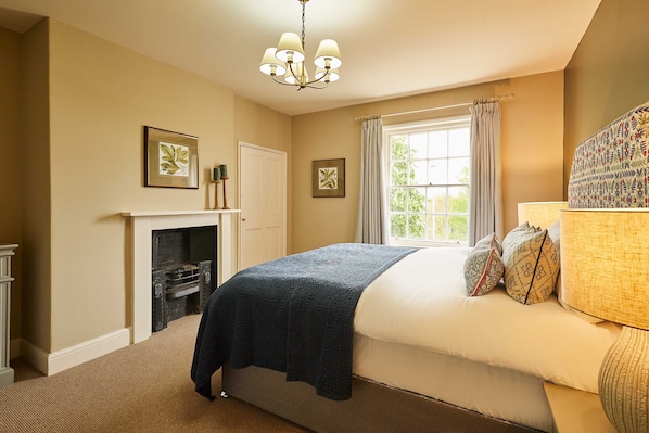 A bedroom with a bed, a fireplace, a window with curtains, and a chandelier. - Host Stay Tree Tops (Darlington)